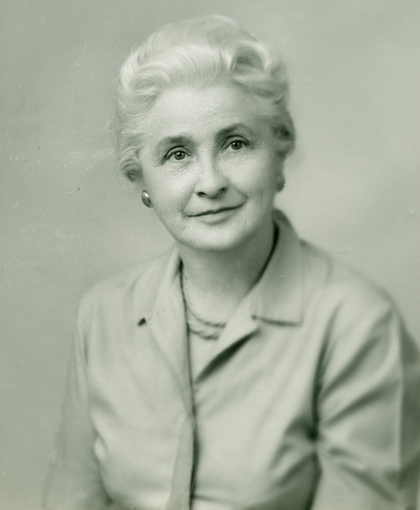 A black and white photo of an older woman with white hair in a button-up top. She's smiling softly towards the camera.